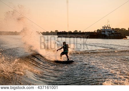 View Of Energy Athletic Male Wakeboarder Riding Water And A Lot Of Splashes Behind Him