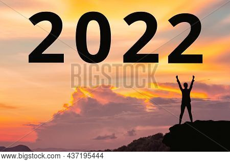 New Year 2022. Silhouette Of Winner Person Standing On The Cliff. Sunset Is On The Background. Conce