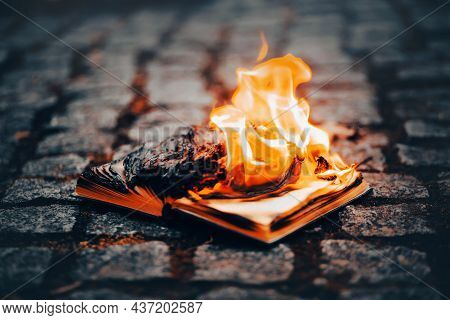 An Open Old Book Lies On The Sidewalk And Burns With A Bright Flame. Book Burning And Censorship. Th