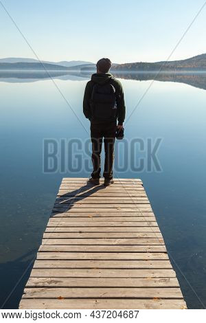 A Man Admires The Landscape Of A Mountain Lake While Standing On The Pier