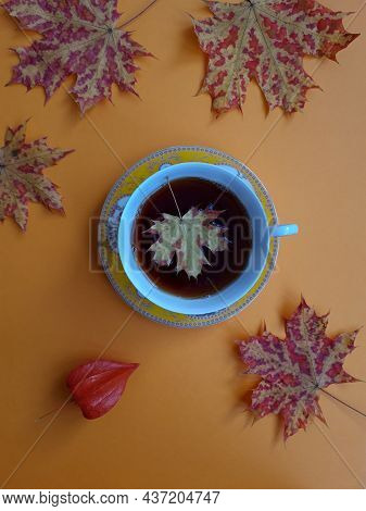 A Cup Of Tea, Maple Leaves, Physalis Flower On An Orange Background.
