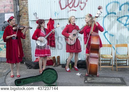 London, Uk - 20 November 2019, A Group Of Girls In Red Robes Play Instruments And Sing At The Flower