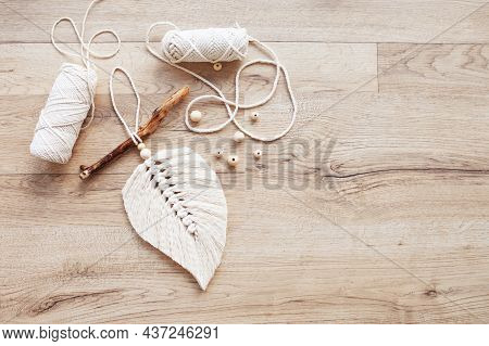 Macrame Leaf  In Natural Color And Thread Windings Lying On A Wooden Table. Cotton Rope Decor Macram
