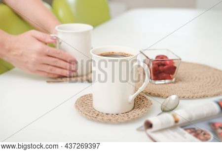 Woman Serving A Coffee In A White Light Kitchen Using Eco Knit Jute Tablemats. Good Morning Concept.