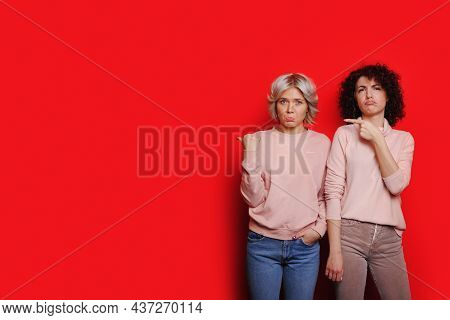 Portrait Of Two Sad Young Women Standing Together And Looking At Camera And Points At Copy Space Iso