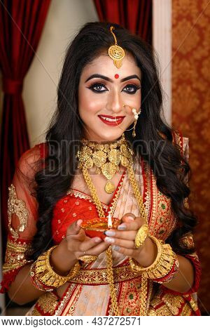 Portrait Of Pretty Young Indian Woman Wearing Traditional Saree, Gold Jewellery And Bangles Holding 