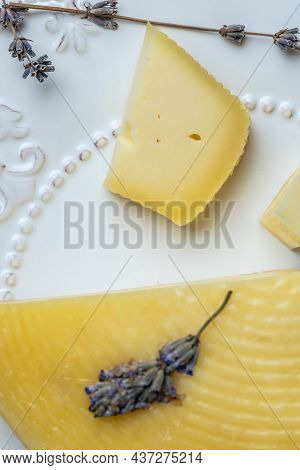A Piece Of Cheese With Herbs On White Plate. Avender Cheese With Dry Basil And Lavender Flowers. Ver
