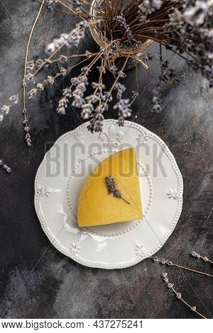 A Piece Of Cheese With Herbs On White Plate. Avender Cheese With Dry Basil And Lavender Flowers. Ver