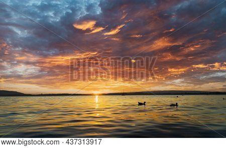 View Of Lake Zugersee From The Swiss Town Of Zug, At Dusk And Calm With The Sun In Front And The Sky