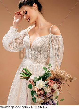Smiling Bride In Gorgeous Wedding Dress With Long Sleeves And Decolletage Holds Trendy Bridal Bouque