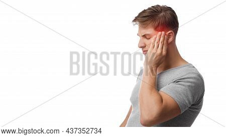 Unhappy Young Caucasian Man Suffering From Headache, Touches His Forehead, Highlighted In Red