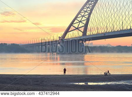 Fisherman On The Beach. Car Bugrinskij Bridge Across The Great Siberian River Ob In The Morning Mist