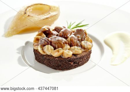 Chocolate tartlet with nuts toffee on white plate. Delicious dessert - Caramel nut tart with pear. Traditional pastry - Butterscotch tartlet with hazelnut, almond and pecan. Autumn dessert