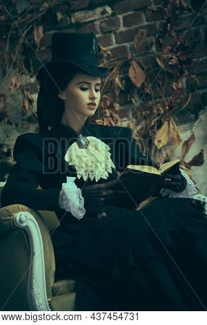 Vintage portrait of a beautiful exquisite young lady of the 19th century reading a book in an armchair. Historical reconstruction of the late 19th and early 20th century.