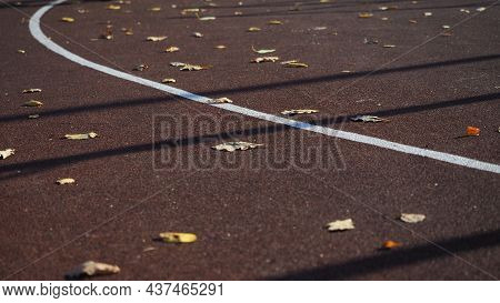 Empty Sports Field With Running Track Markings Used In Outdoor Tennis In Autumn With Fallen Leaves. 