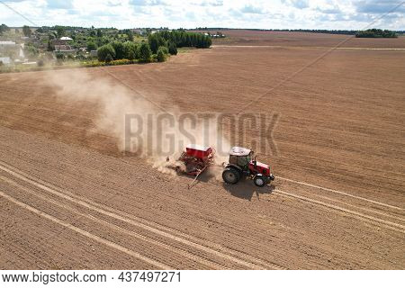 Agricultural Tractor Sowing Seed Onto At Field. Farming And Seeding Concept. Seeds Sowing In Farmers