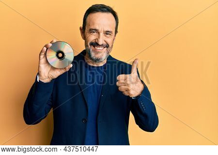 Middle age hispanic man holding compact disc smiling happy and positive, thumb up doing excellent and approval sign 