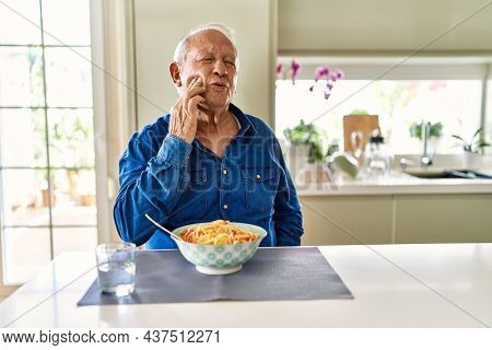 Senior man with grey hair eating pasta spaghetti at home touching mouth with hand with painful expression because of toothache or dental illness on teeth. dentist 
