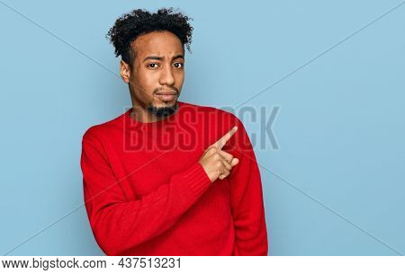 Young african american man with beard wearing casual winter sweater pointing aside worried and nervous with forefinger, concerned and surprised expression 