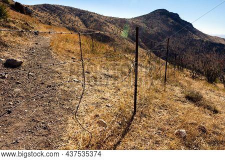 Fence Made Of Barbed Wire Delimiting Mountains Covered In Dried Plants From A Steppe Climate.