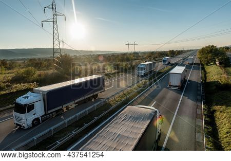 Convoys Or Caravans Of Transportation Trucks Passing On A Highway At Sunset. Highway Transit Transpo