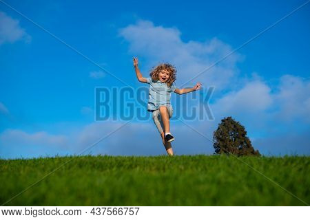 Little Adorable Boy Running On Grass. Excited Kid Play The Green Grass. The Child Has Blond Long Hai