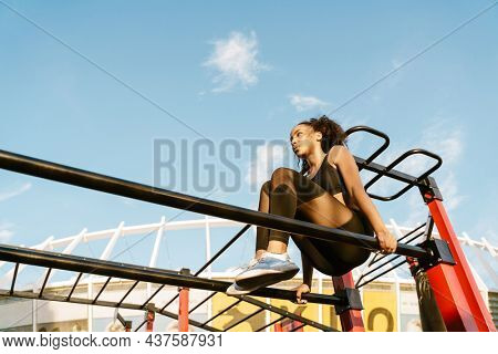 Concentarted young fit african fitness woman exercising on parallel bars at the sportsground
