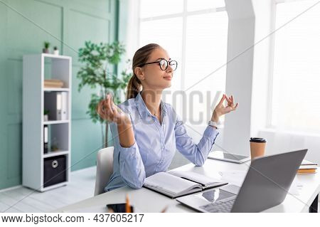 Coping With Stress At Work. Young Female Entrepreneur Meditating At Workplace, Doing Breathing Exerc