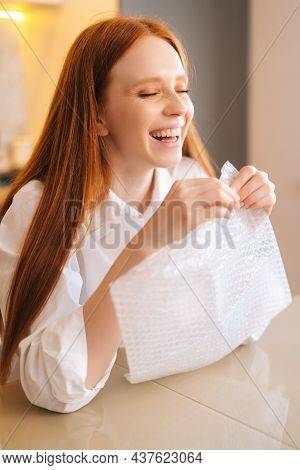 Close-up Vertical Shot Of Laughing Young Woman Playing Pops Bubble Wrap To Calm Herself Sitting At T