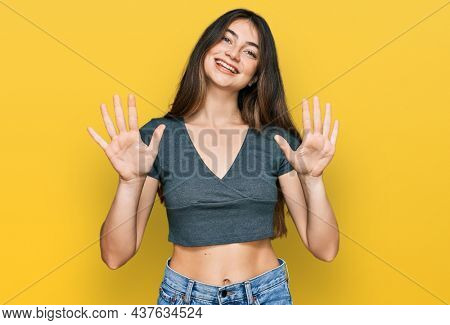 Young beautiful teen girl wearing casual crop top t shirt showing and pointing up with fingers number ten while smiling confident and happy. 
