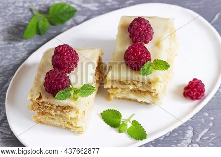 Pieces Of Napoleon Cake Decorated With Raspberries And Lemon Balm Leaves On A Light Background.