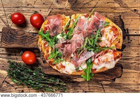 Sliced Pizza With Prosciutto Parma Ham, Arugula And Parmesan Cheese On A Wooden Board. Wooden Backgr