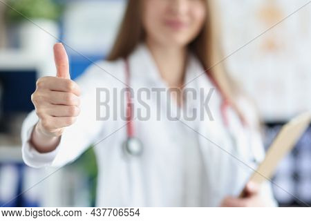 Focus On Practitioner Hand Demonstrating Approval Thumb Up Gesture. Woman Therapist In White Gown Wi