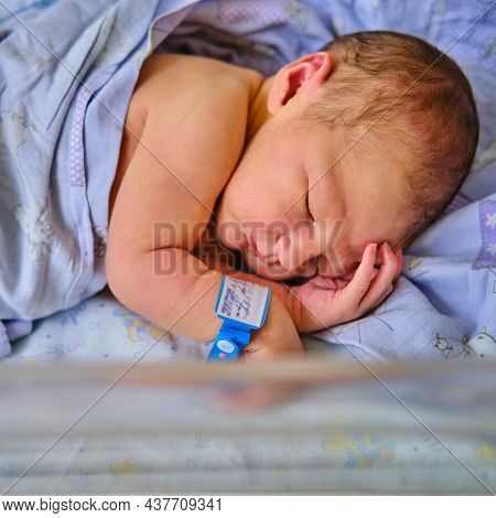 A Newborn Baby With A Maternity Hospital Bracelet On His Arm Is Sleeping In A Crib. A Newly Born Chi