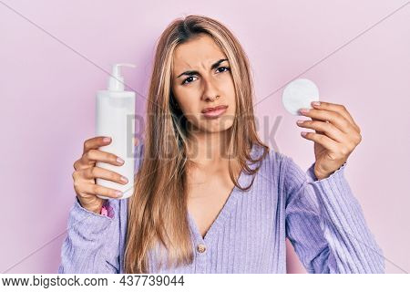 Beautiful hispanic woman holding cotton pad and make up remover clueless and confused expression. doubt concept. 