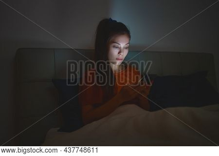 Woman sleeping using phone in bed staying up late at night reducing her sleep time which is bad for mental health and depression.