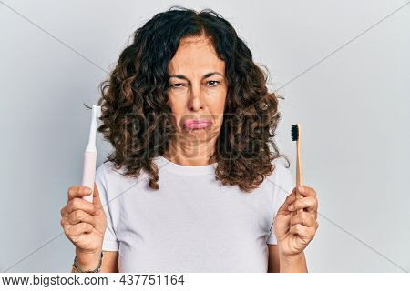 Middle age hispanic woman holding electric toothbrush and teethbrush depressed and worry for distress, crying angry and afraid. sad expression. 