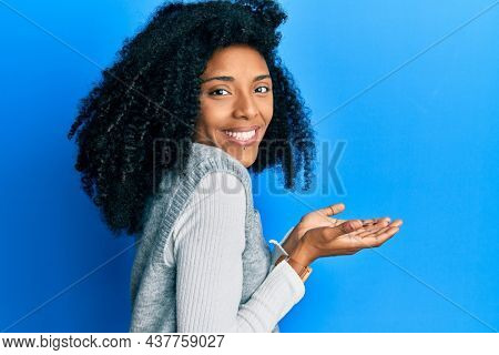 African american woman with afro hair wearing casual winter sweater pointing aside with hands open palms showing copy space, presenting advertisement smiling excited happy 