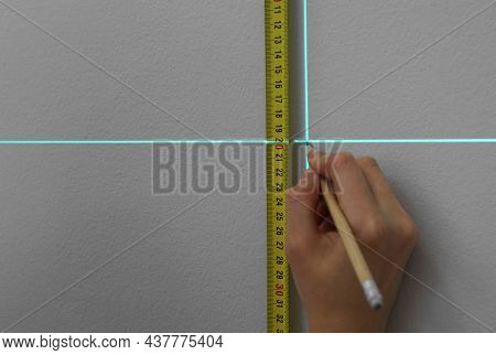 Woman Using Cross Line Laser Level, Tape And Pencil For Accurate Measurement On Grey Wall, Closeup