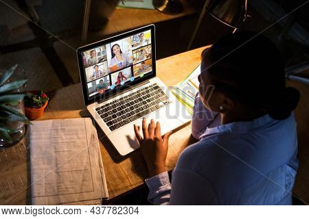 African american woman using laptop for video call, with diverse elementary school pupils on screen. communication technology and online education, digital composite image.