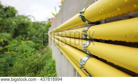 Clamps And Conduits On The Side Of The Wall. Rows Of Many Yellow Conduits Are Beside The Cement Wall