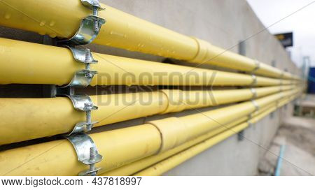Clamps And Conduits On The Side Of The Wall. Rows Of Many Yellow Conduits Are Beside The Cement Wall