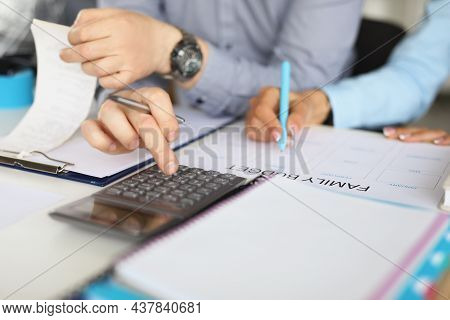 Close-up Of Couple Planning Family Budget For Month. Man Counting On Calculator, Woman Write Down On