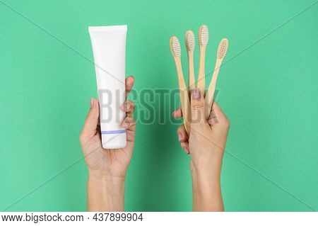 Bamboo Toothbrushes And A Tube Of Toothpaste In Female Hands On A Mint Background. Current Trends In