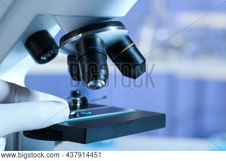 Scientist Examining Sample Of Light Blue Liquid On Slide Under Microscope In Laboratory, Closeup