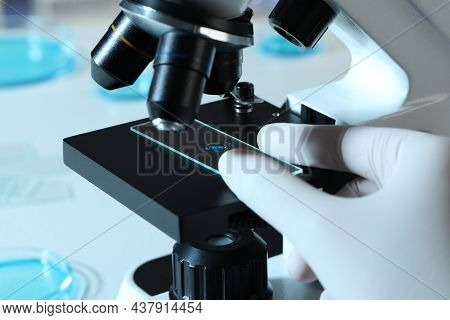 Scientist Examining Sample Of Light Blue Liquid On Slide Under Microscope In Laboratory, Closeup