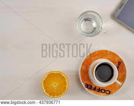 A Cup Of Coffee, An Orange, A Glass Of Water On A Wooden Background. Coffee Break. Snack. Top View. 