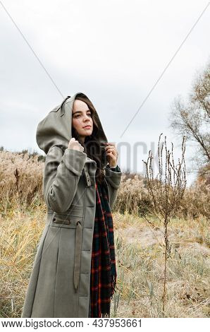 Young Dreamy Woman With A Hood On Standing In The Dry Grass Field Looking Away During Autumn Season.