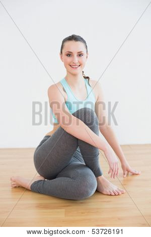 Full length portrait of a fit young woman sitting in cowface posture against wall in fitness studio