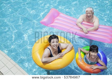 Multi-generational family playing in pool with inflatable tubes